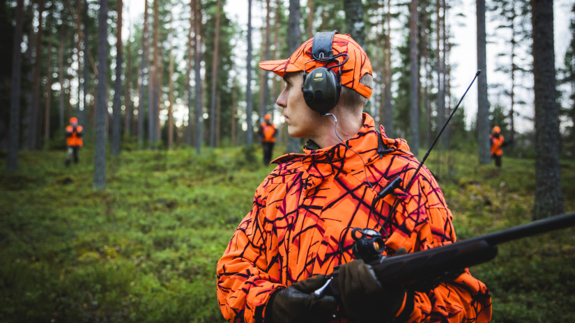 Metsästäjä jolla kuulosuojaimet, huomiovaatetus ja ase.