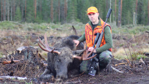 Nuori metsästäjä kaatamansa hirven vieressä.
