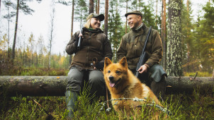 Två jägare och en finsk spets tar en paus i skogen.